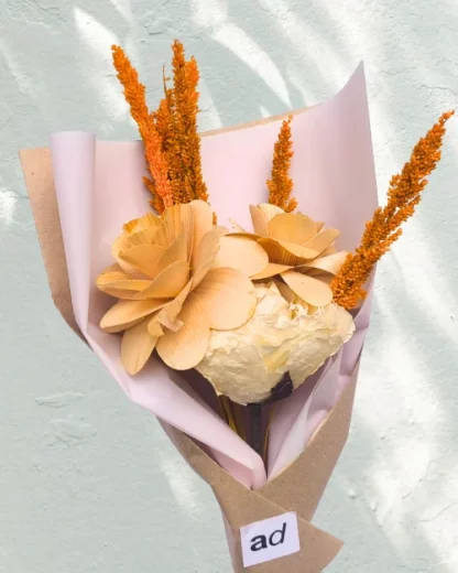 A mini flower bouquet with 2 wooden roses and fossilized stem white rose wrapped in a light pink colored paper.