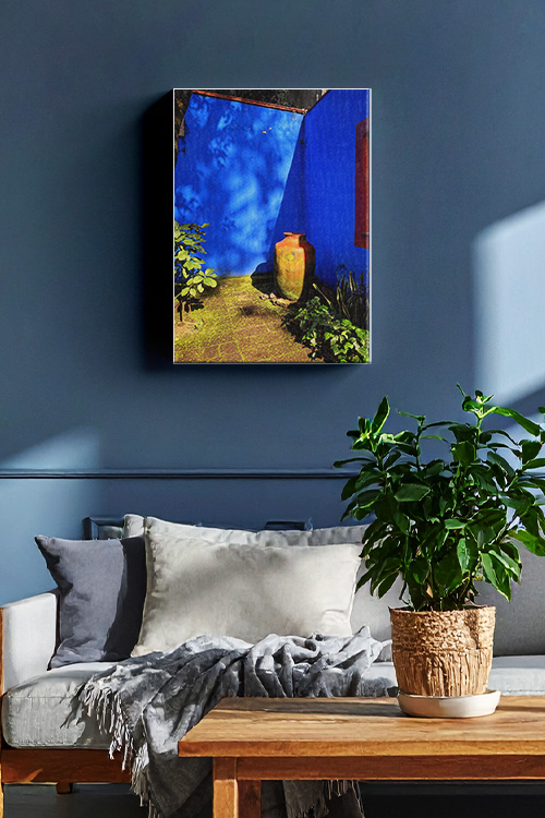 A canvas art print of a blue wall and an old vase in Casa Azul, Mexico displayed on a living room with a blue-colored wall